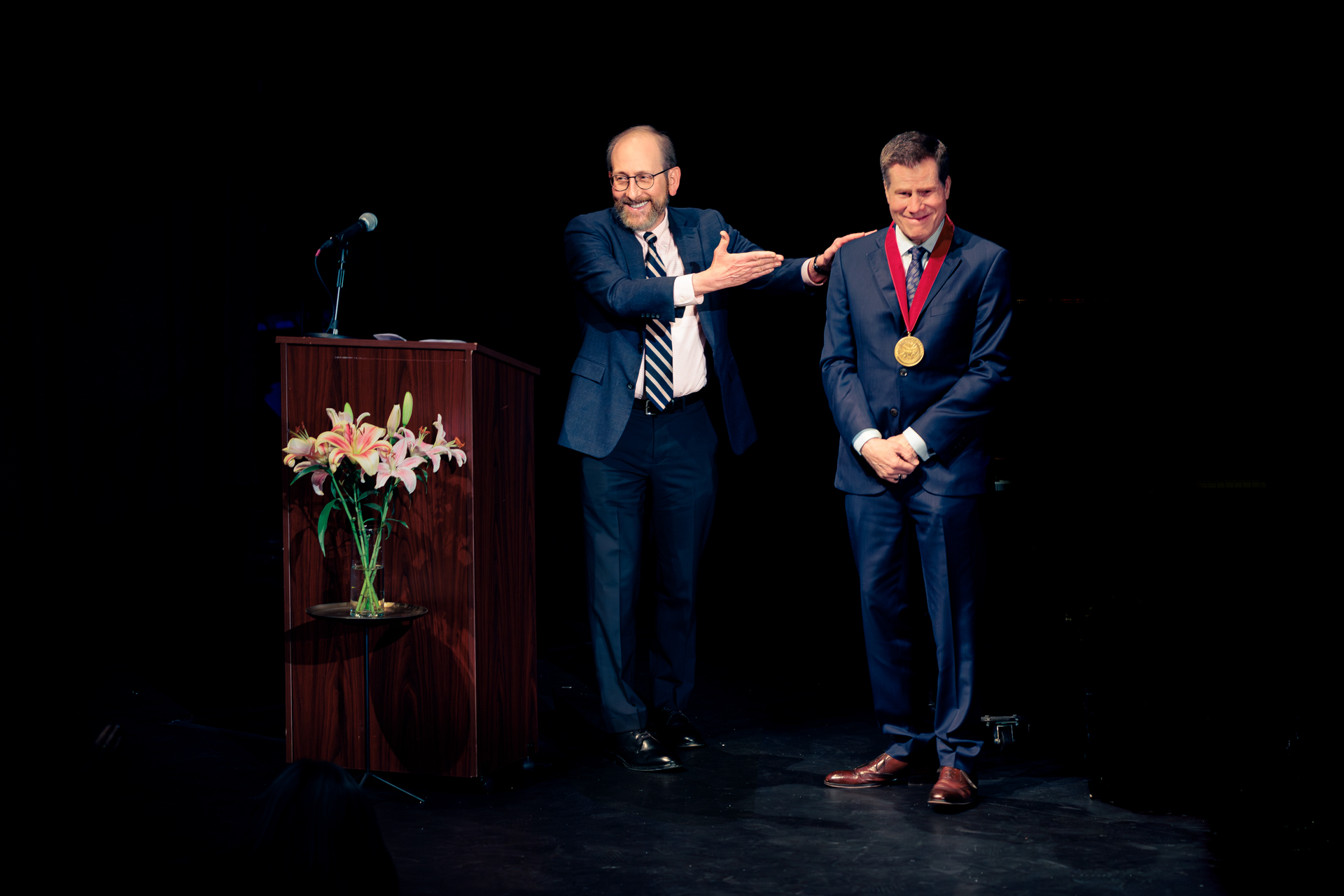 Harvard President Alan Garber, at left, presented theater director Bill Rauch with the 2026 Harvard Arts Medal in a ceremony Sunday at Farkas Hall.