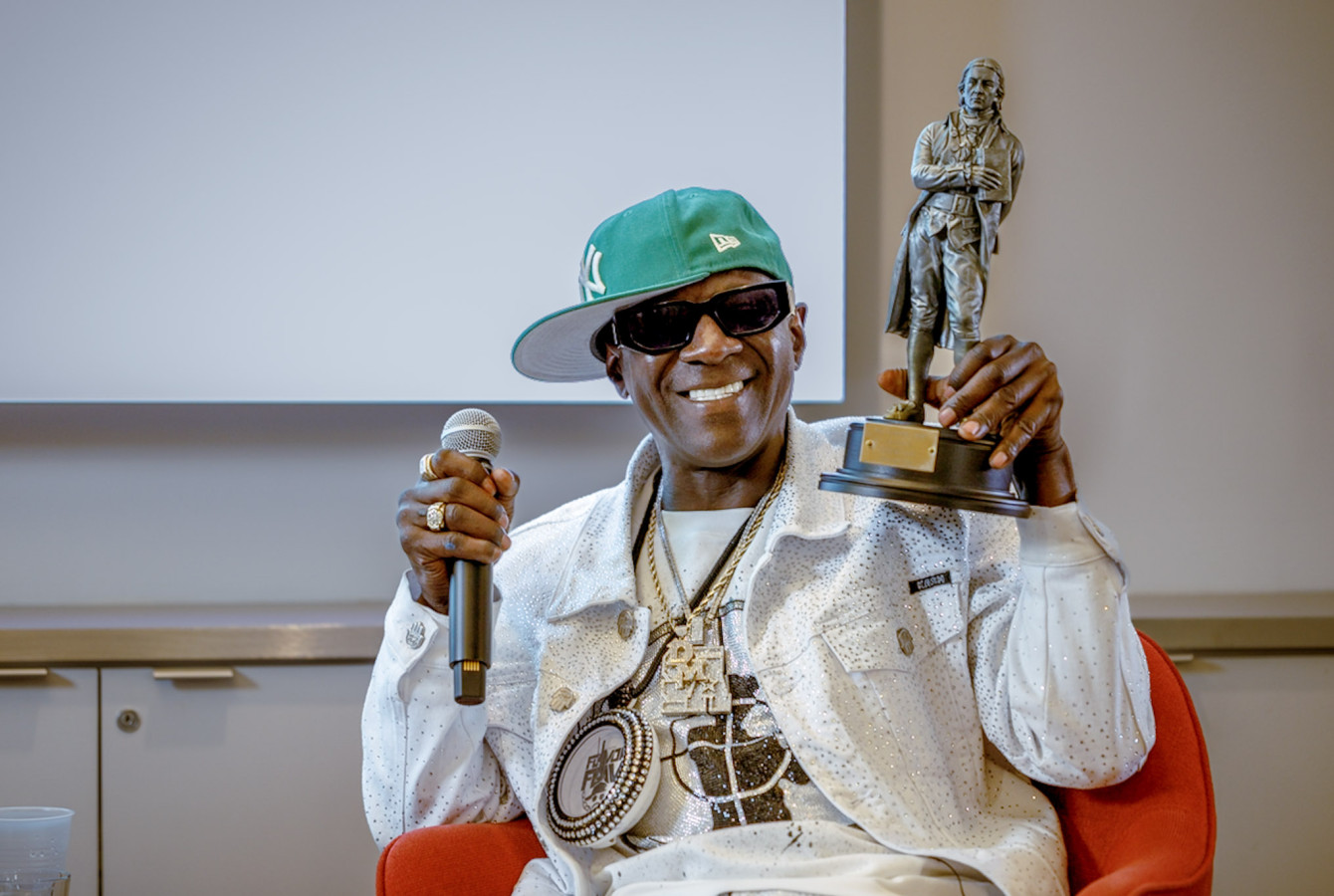 Flavor Flav received a John Harvard statue, which he raised for the audience to see, during an appearance at Harvard University’s Marcyliena H. Morgan Hip Hop Archive & Research Institute.
