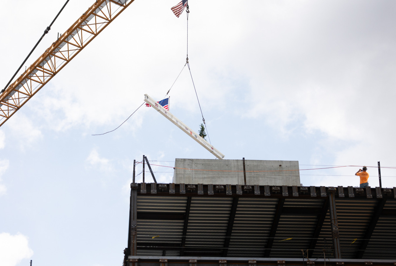 A crane hoists a steel beam atop a building frame