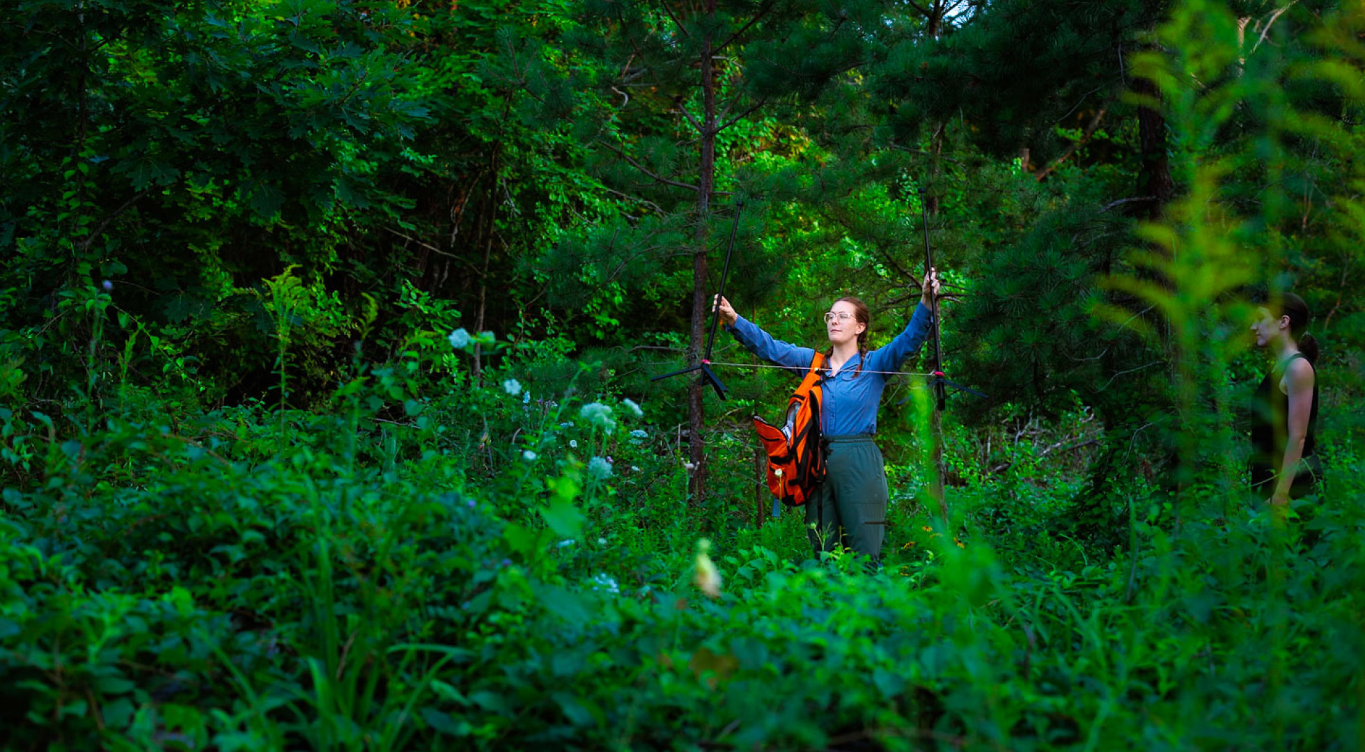 Abby Robinson in a blue shirt in a field, arms outstretched, placing two GoPro cameras