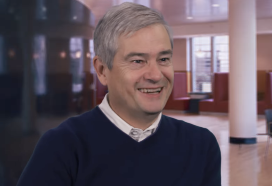 Professor Steve Ansolabehere smiles wearing a collared shirt and sweater