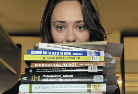 Natalie Behrends peeking out from behind a stack of books about socialism