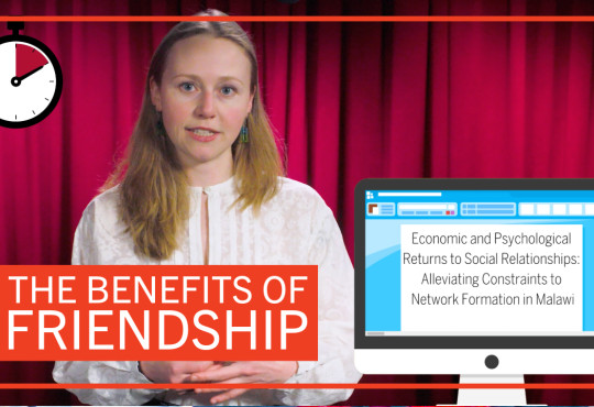 Student Gabriella Fleischman in front of a red curtain with graphics reading “The Benefits of Friendship” and ”Economic and and Psychological Returns to Social Relationships: Alleviating Constraints to Network Formation in Malawi”