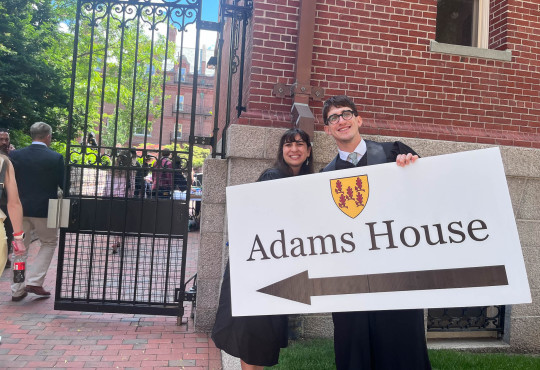 Adams House resident tutors Sarah Gonzalez and Francesco Rolando hold a sign with a giant arrow to direct visitors to the House's diploma ceremony.