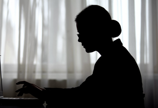 Silhouette of a woman sitting alone in a dark home office