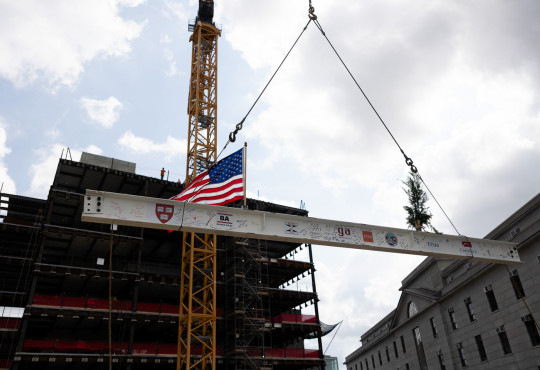 A crane hoists a steel beam atop a building frame.