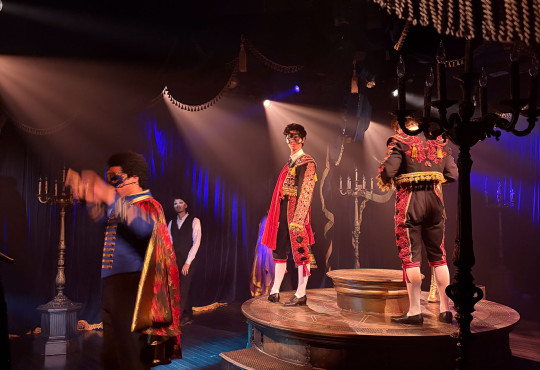 Tanner Quirk performs as Young Phantom in costume on a circular stage during the immersive theater production “Masquerade.”