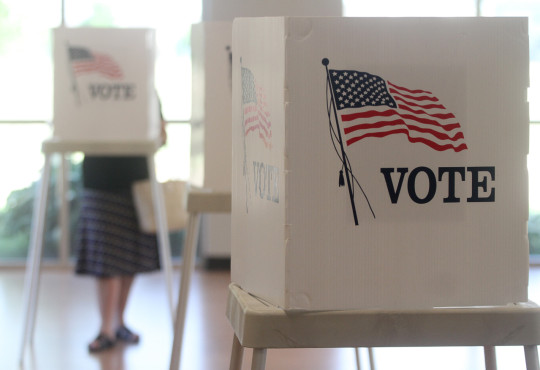 A U.S. polling booth is shown in close-up, with more booths appearing in the background