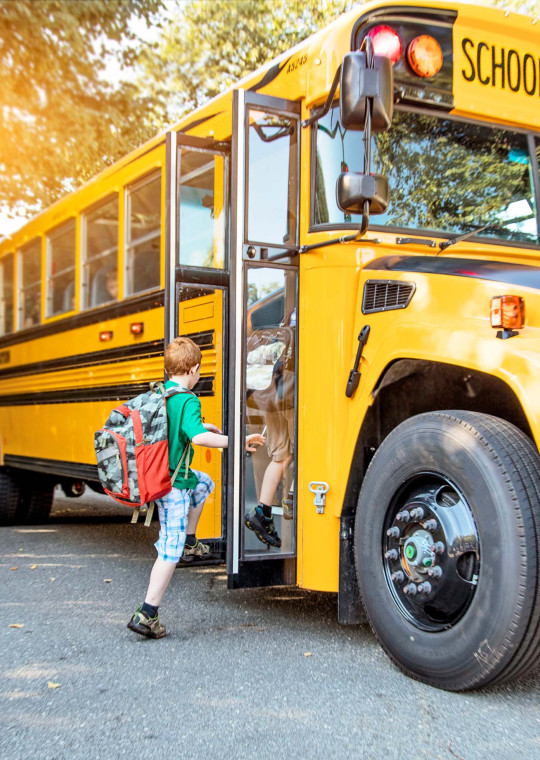 A child wearing a backpack boarding a school bus