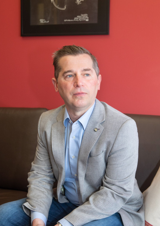 Psychology professor Matthew Nock seated on a gray couch in front of a red wall