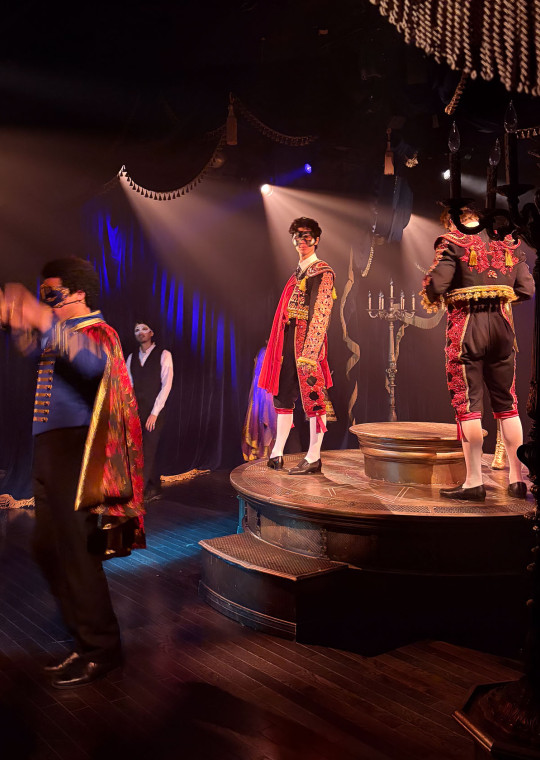 Tanner Quirk performs as Young Phantom in costume on a circular stage during the immersive theater production “Masquerade.”