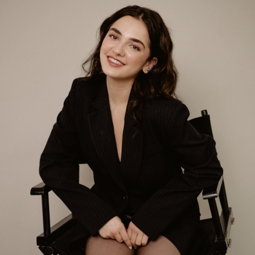 Mattea Conforti ’28 smiles in a director's chair, wearing a black pinstripe blazer.
