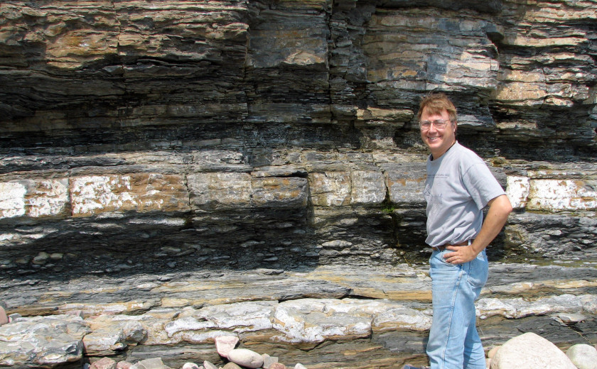 Andrew Knoll standing in front of a vibrant formation of geological strata
