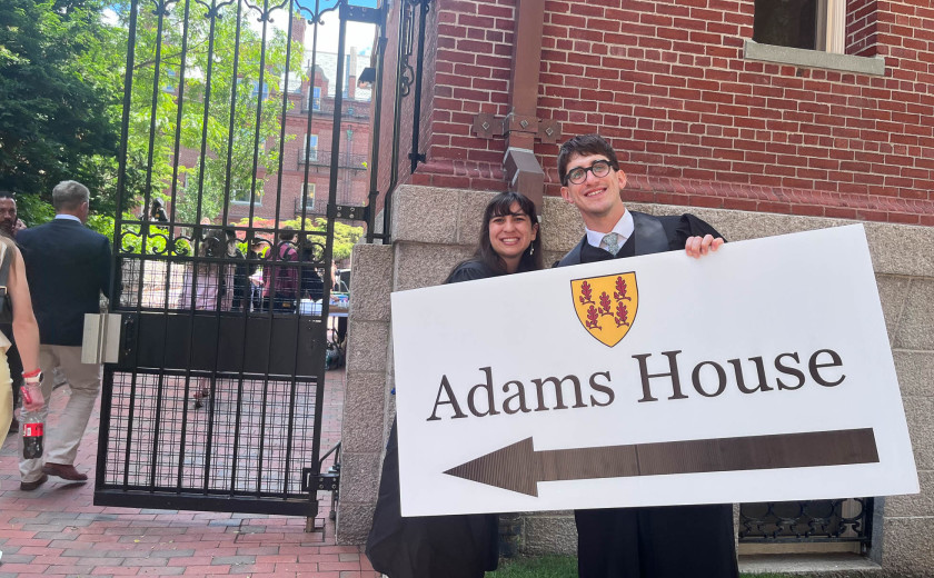 Adams House resident tutors Sarah Gonzalez and Francesco Rolando hold a sign with a giant arrow to direct visitors to the House's diploma ceremony.