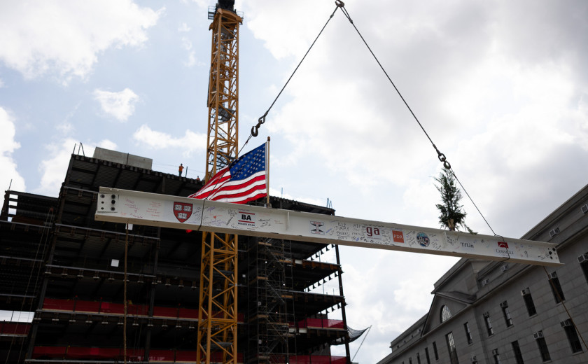 A crane hoists a steel beam atop a building frame.