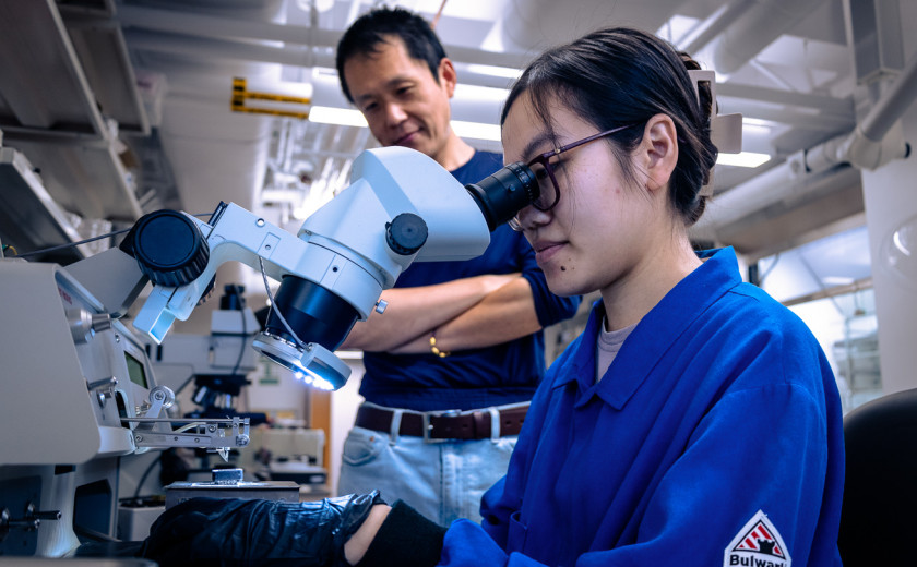 Graduate student Thao Dinh peering into a microscope while professor Suyang Xu looks on