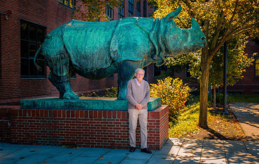 Molecular biologist Rich Losick posing by one of the 3-ton bronze rhinoceros sculptures in front of the Bio Labs